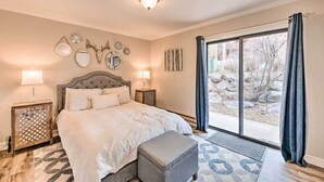 Ein Schlafzimmer mit einem großen Bett, zwei Nachttischen, einem Fenster mit Vorhängen und Blick ins Freie.
