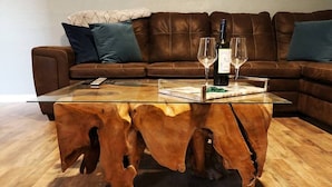 Ein Couchtisch mit Glasplatte und Holzfuß, eine Weinflasche und zwei Weingläser auf Holzboden.