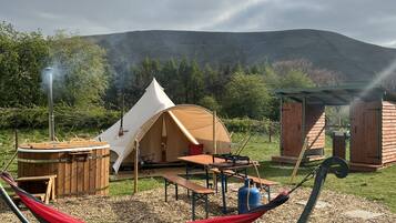 A campsite with a tent, a wooden hot tub, a hammock, and a barbecue area.