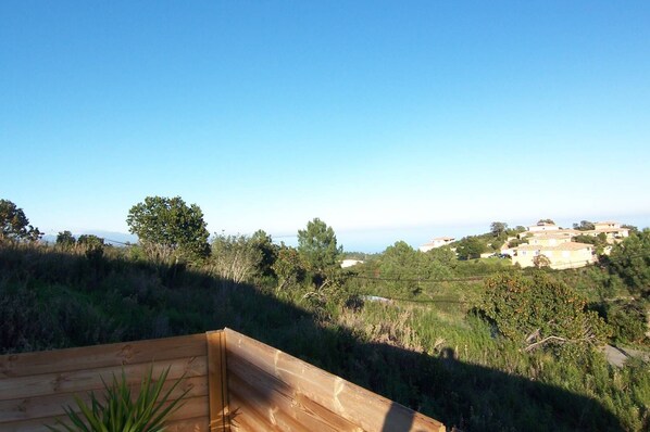 Eine Holzterrasse mit Blick auf eine Hügelslandschaft, im Hintergrund sind Gebäude zu sehen.