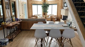 Una cocina amplia con detalles de madera, un comedor con sillas blancas y un rincón de descanso acogedor con un sofá y una planta.
