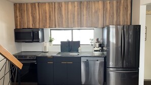Una cocina moderna con refrigerador de acero inoxidable, microondas, cafetera y armarios de madera.