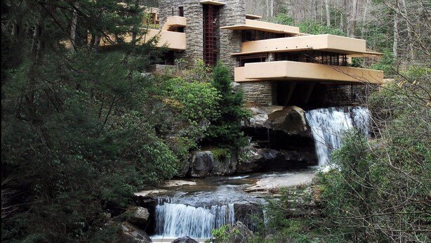 Un edificio moderno con fachada de piedra y varios balcones con vistas a una cascada.