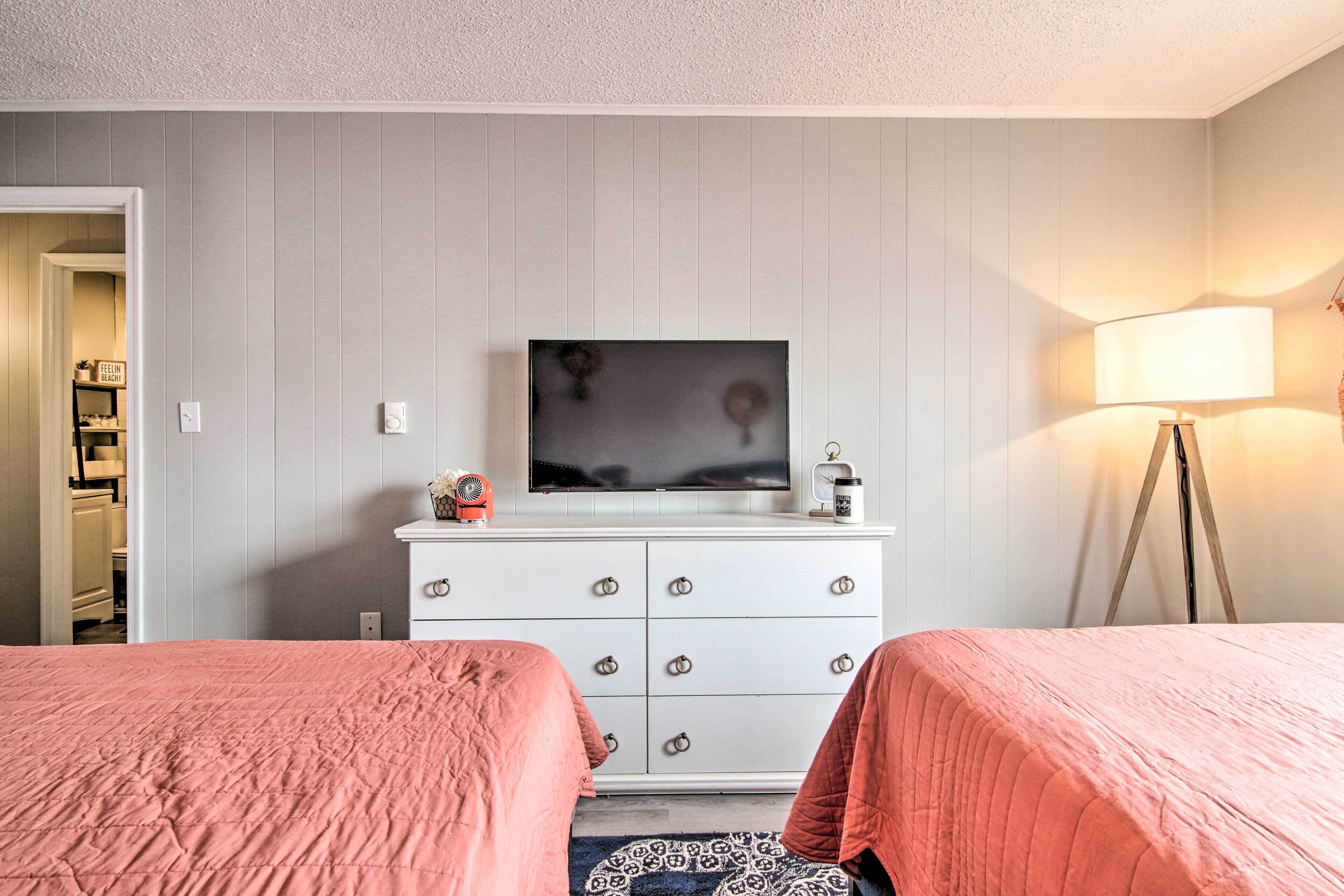 Hotellihuone, jossa on kaksi sänkyä, valkoinen lipasto, taulutelevisio, lamppu ja kuviollinen matto.