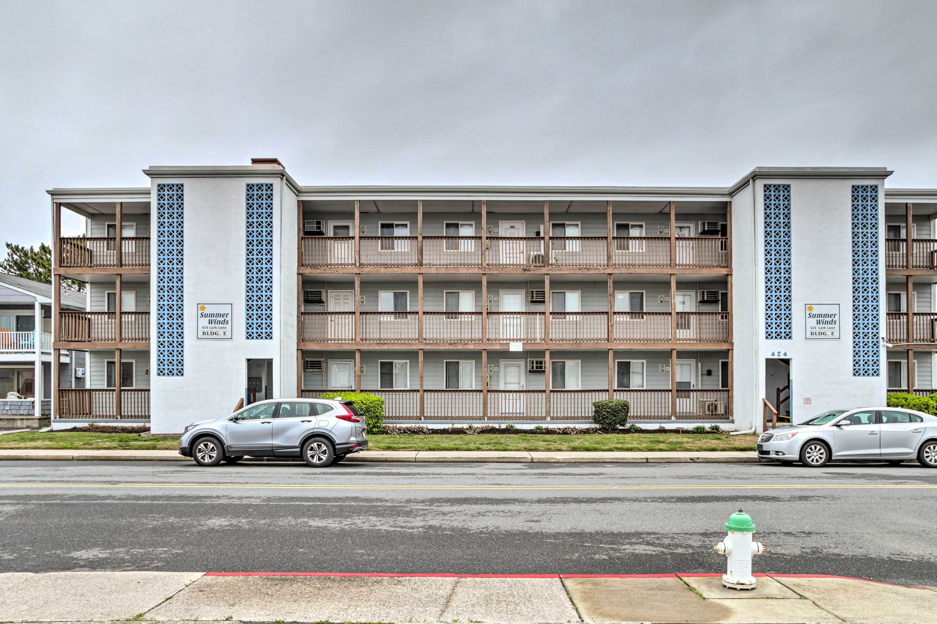 A multi-story hotel with balconies, a fire hydrant on the sidewalk, and cars parked in front.