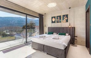 A modern bedroom with a large bed, a view of the outdoors, and a dining area with a glass wall. - Villa with pool and spa (Baška)