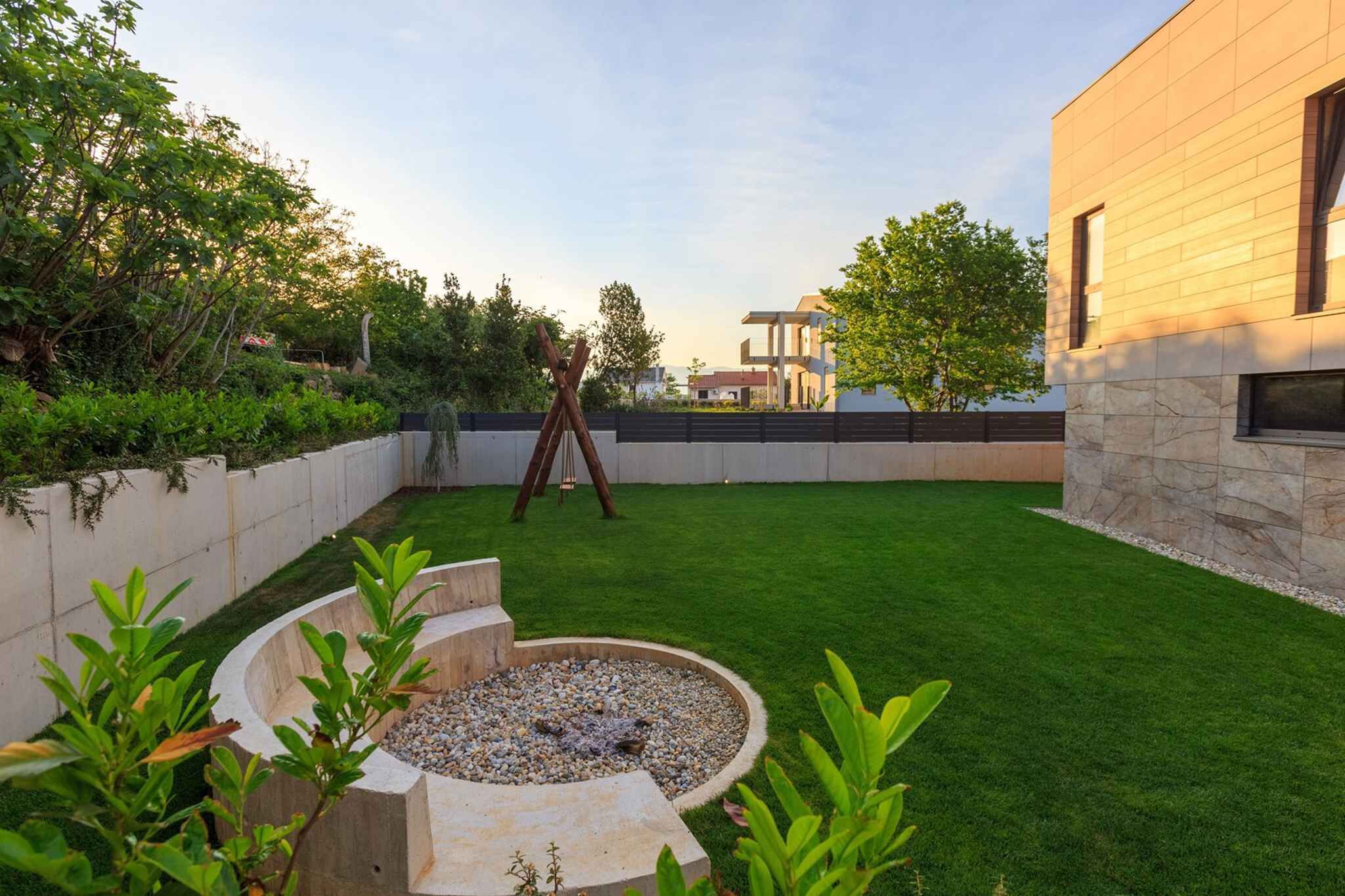 A modern outdoor patio with a circular seating area, a wooden swing set, and a well-maintained lawn.