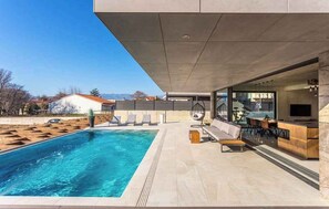 A modern outdoor pool area with a bar and seating, clear skies, and distant mountains. - Villa with pool and spa (Baška)