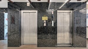Zona de ascensores moderna con paredes de mármol y un cartel de 'NO FUMAR'.