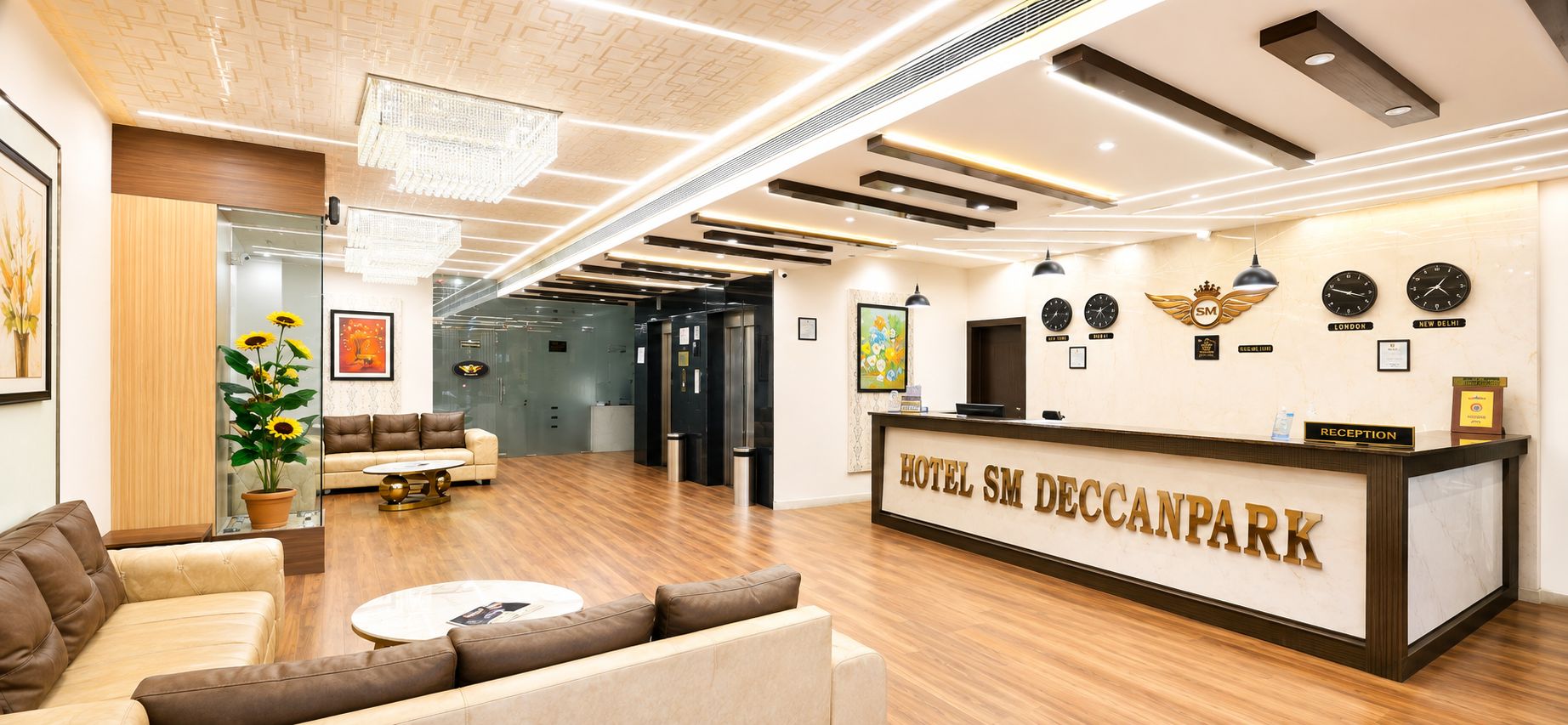 A hotel reception area with a reception desk, sofas, a coffee table, and a wall with clocks and awards.