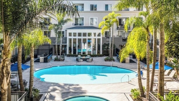 A swimming pool surrounded by palm trees and outdoor seating areas, with a building in the background. - Cute Poolside Unit, 2 Miles from the Beach (Marina del Rey)