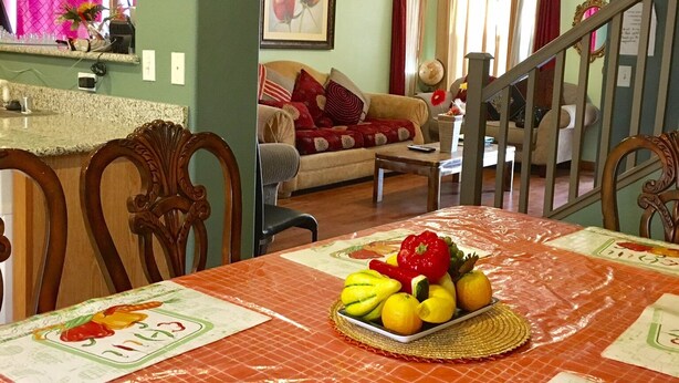 A dining area with a table set for a meal, a kitchen in the background, and a staircase leading upstairs.