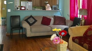 A living room with a sofa, a coffee table with flowers, and a kitchen in the background.