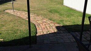 A backyard with a brick pathway leading to a white building. - Cute country cottage in Cessnock (Cessnock)