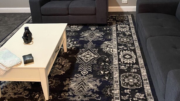A living room with a dark grey sofa, a matching armchair, a patterned rug, and two large floral paintings on the wall. - Cute country cottage in Cessnock (Cessnock)