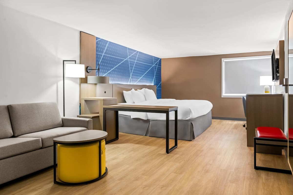 Una habitación de hotel con cama, sofá, mesita, lámpara y televisor.