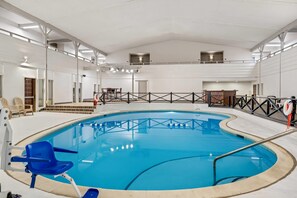 A large indoor swimming pool with a clear blue water, surrounded by a black safety fence, and equipped with a lifebuoy.