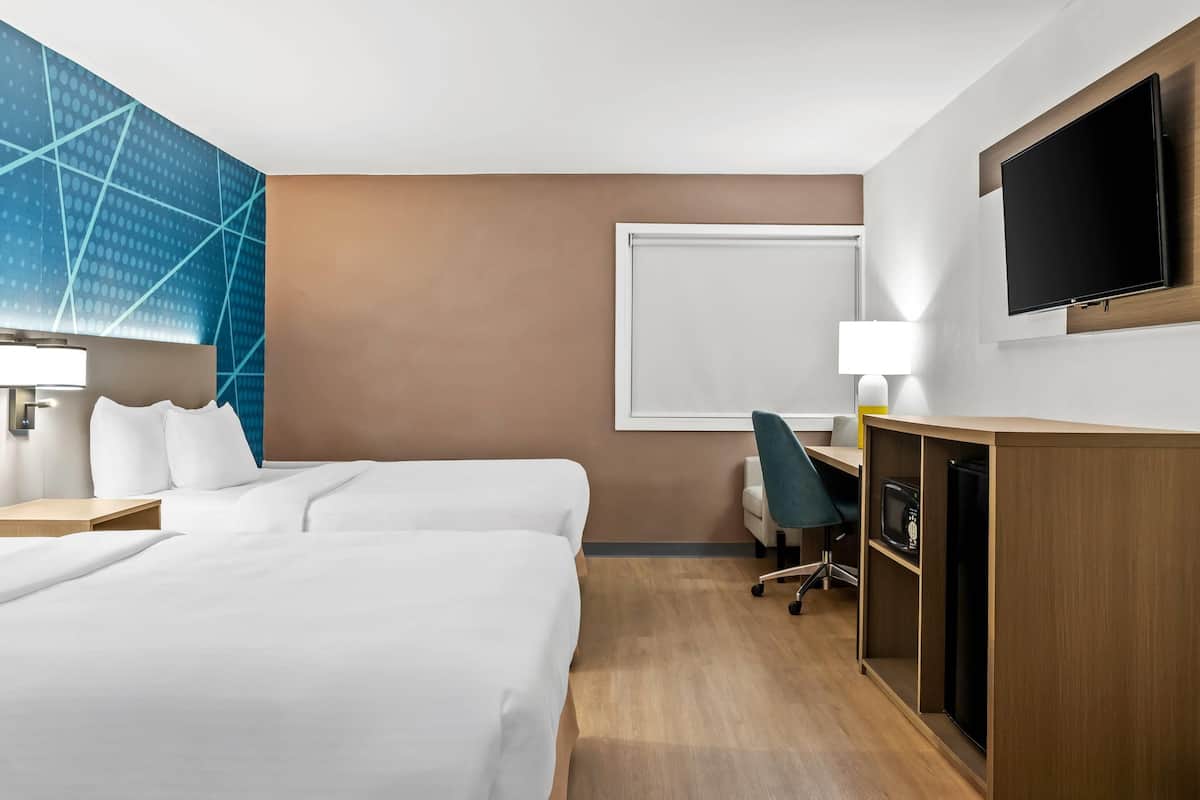 Habitación de hotel con dos camas, un escritorio con silla, un televisor y un ventanal amplio.