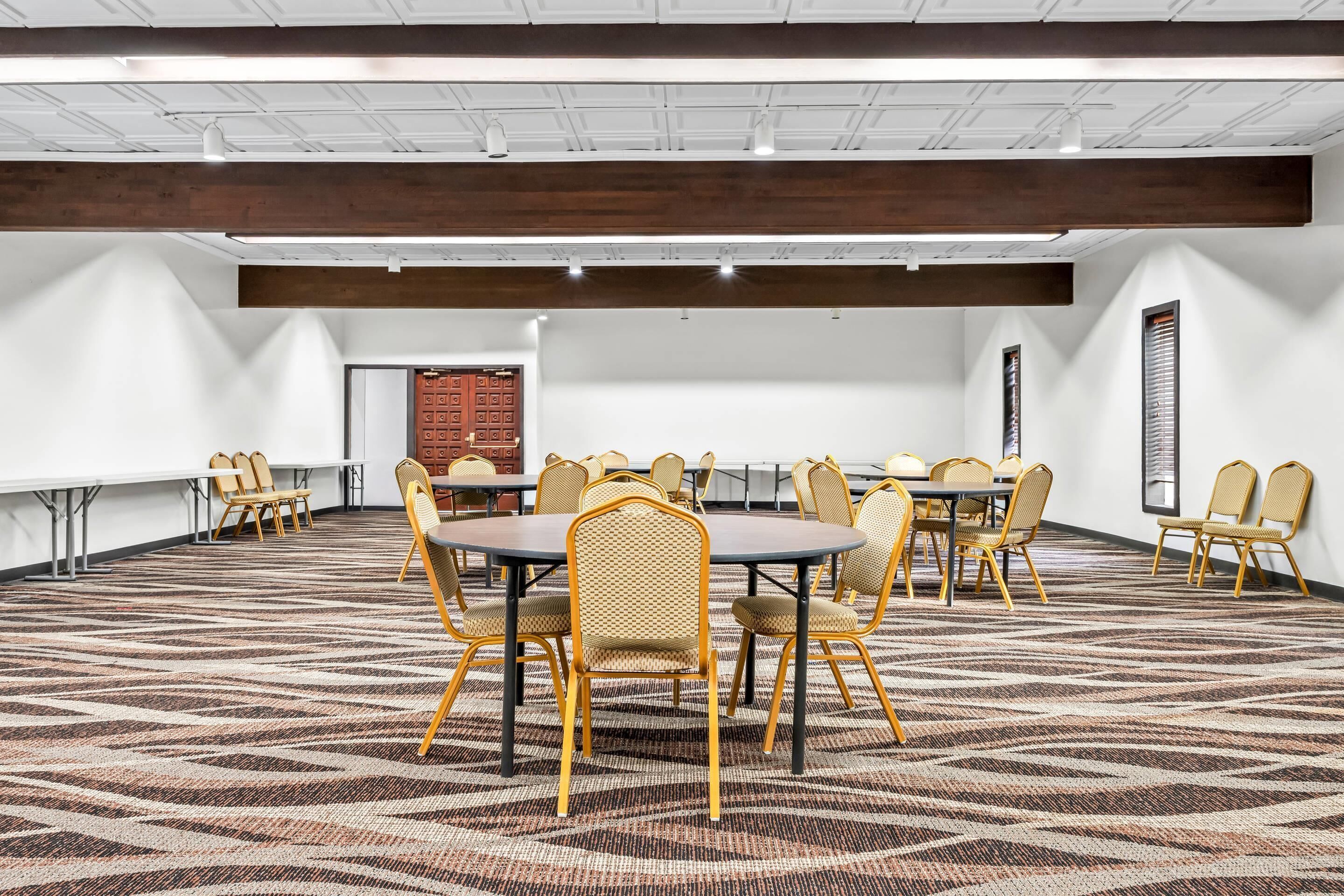 A conference room with round tables and chairs, white walls, and a patterned carpet.