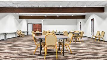 A conference room with round tables and chairs, white walls, and a patterned carpet.