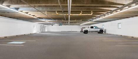 A parking garage with concrete ceilings, fluorescent lighting, and a white car parked in one of the spaces.