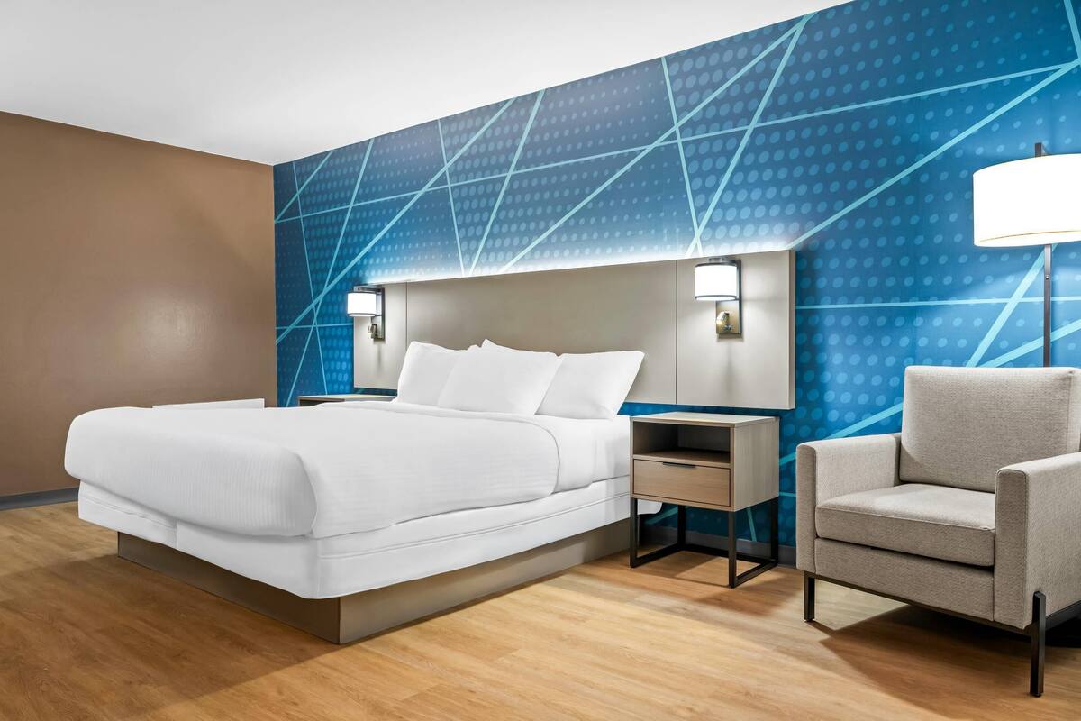 Una habitación de hotel moderna con una cama grande, mesitas de noche, una silla y una pared con estampado azul.