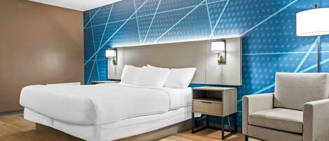 A modern hotel room with a large bed, bedside tables, a chair, and a blue patterned wall.