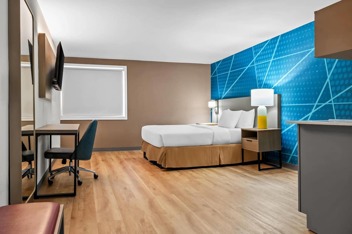 Habitación de hotel con cama, escritorio, silla y un amplio ventanal.