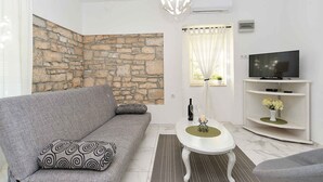 Ein Wohnzimmer mit Steinwand, einem grauen Sofa, einem weißen Couchtisch, einem Fernseher auf einem weißen Schrank und einem Fenster mit Vorhängen.