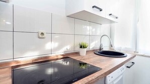 Eine moderne Küche mit weißen Fliesen, einer schwarzen Induktionskochplatte, einer Holzarbeitsplatte, einem Spülbecken und einem Blumentopf.