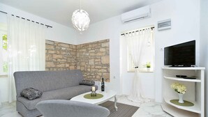 Ein modernes Wohnzimmer mit grauem Sofa, rundem Couchtisch, Fernseher auf weißem Lowboard und einer Steinwand.