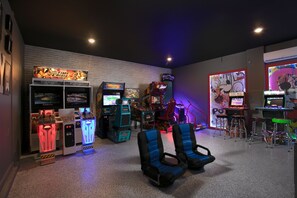 Ein Raum mit Spielautomaten, darunter 'Time Crisis' und 'Wii Sports', sowie zwei blaue Gaming-Stühle.