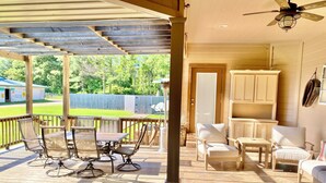A covered patio with a table and chairs, a seating area with a sofa and armchairs, and a ceiling fan.