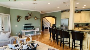 A spacious living area with a wooden dining table, bar stools, and a kitchen with cream-colored cabinets.