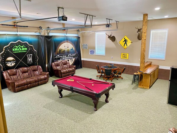 Une pièce équipée d’une table de billard, de canapés en cuir, d’un bar en bois et d’un écran de projection.