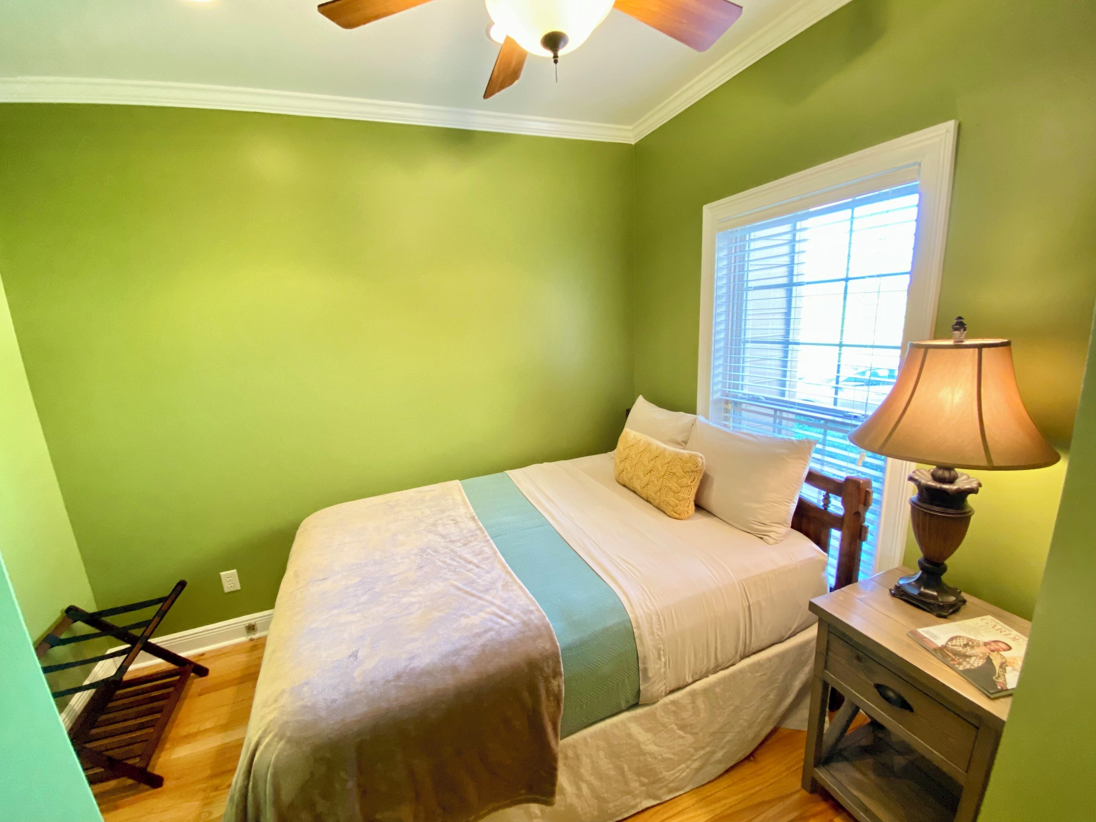A bedroom with a bed, a nightstand, a lamp, a window with blinds, and a ceiling fan.