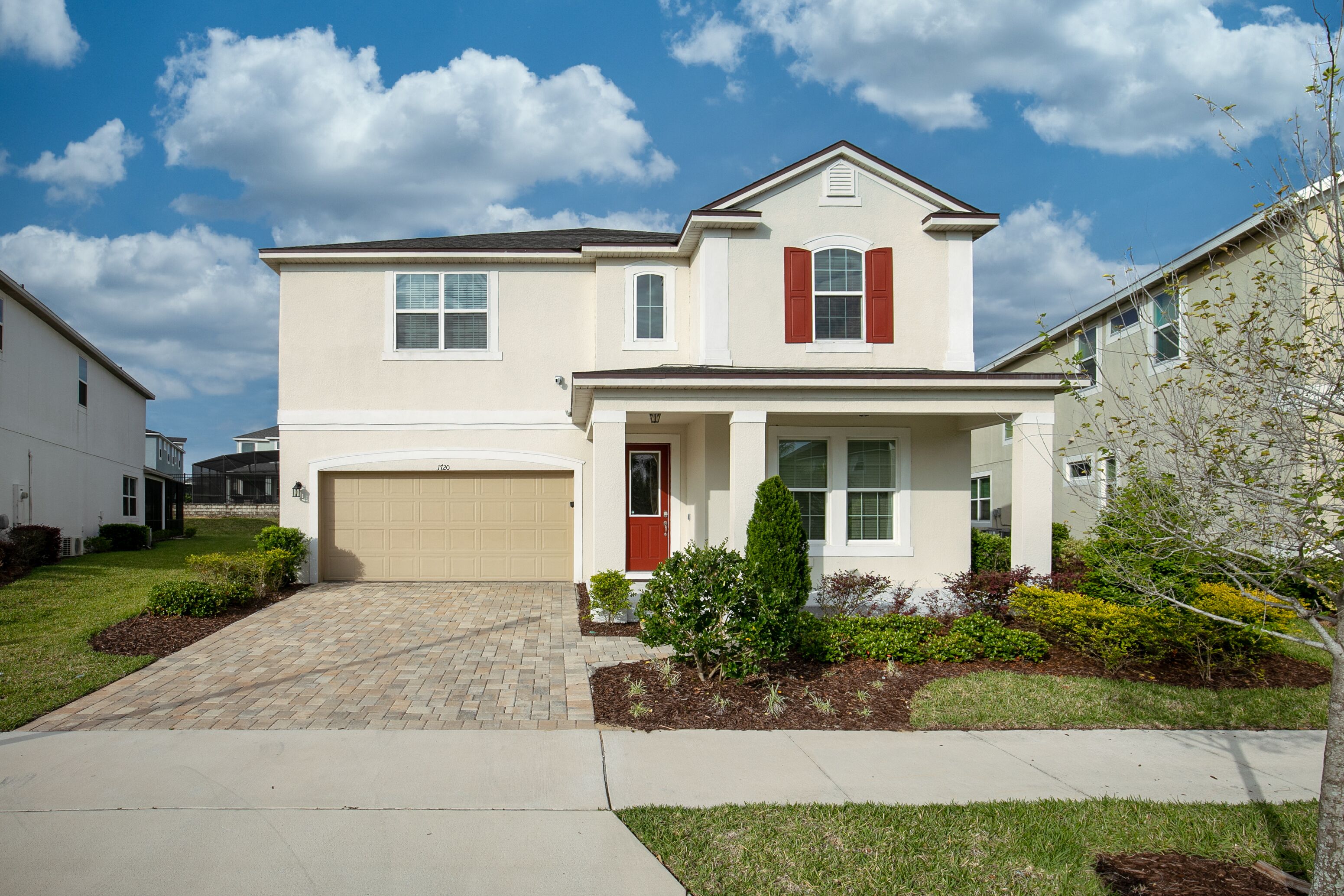 A two-story residential house with a beige exterior, a red door, and a garage.