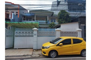Un coche amarillo aparcado frente a una zona residencial cerrada con un portón blanco y detalles metálicos decorativos.