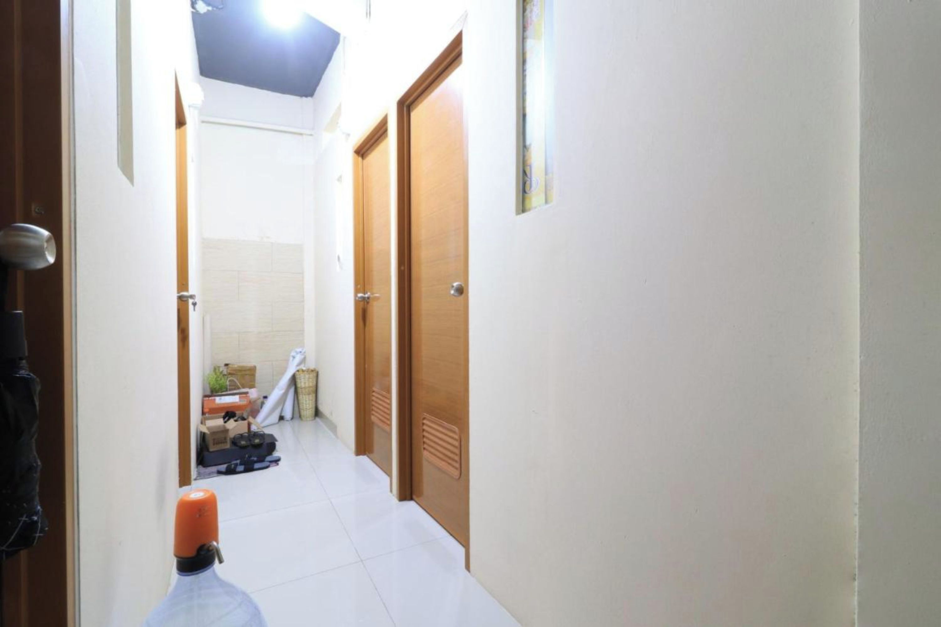 A narrow hallway with white tiled floors and wooden doors.