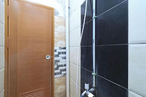 Een badkamer met een houten deur, betegelde wanden en een zichtbare sanitaire voorziening.