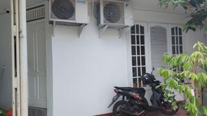 Un bâtiment avec deux unités de climatisation fixées sur le mur extérieur, une moto garée devant et une porte donnant sur l’entrée.