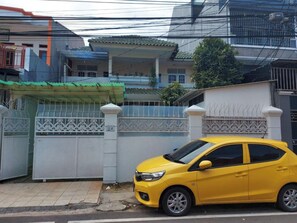 Une voiture jaune est garée devant un lotissement privé, dont l’entrée est marquée par un portail blanc agrémenté d’éléments décoratifs en métal.
