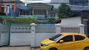 Une voiture jaune est garée devant un lotissement privé, dont l’entrée est marquée par un portail blanc agrémenté d’éléments décoratifs en métal.
