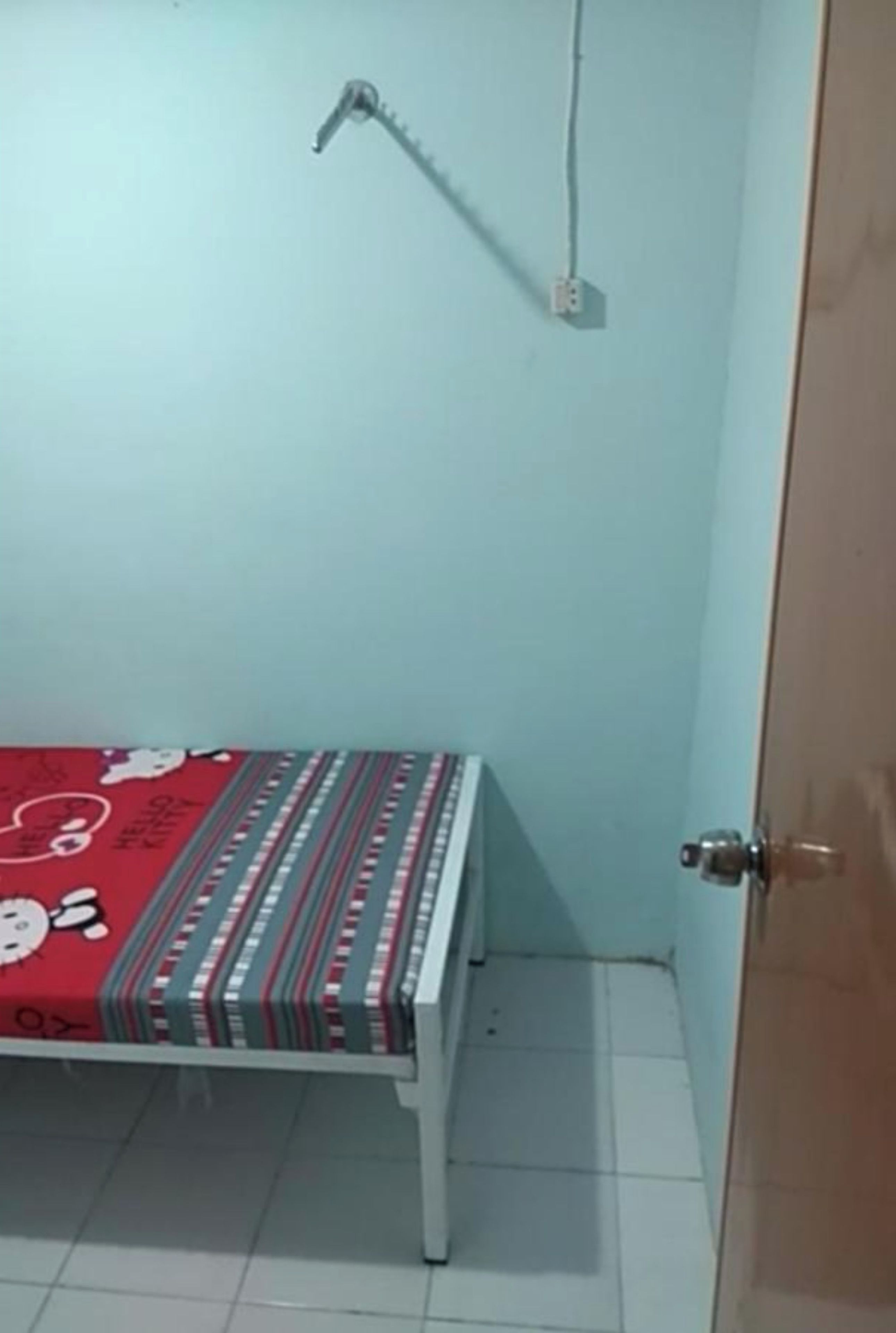 A small room with a bed, a door, and a wall socket.
