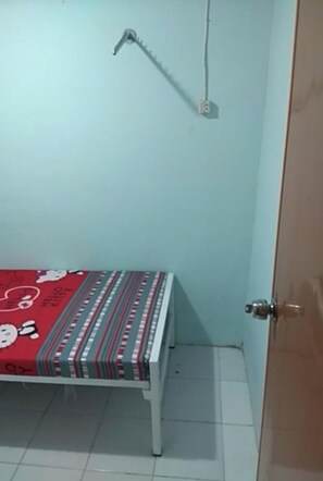 Une petite pièce avec un lit, une porte et une prise électrique.