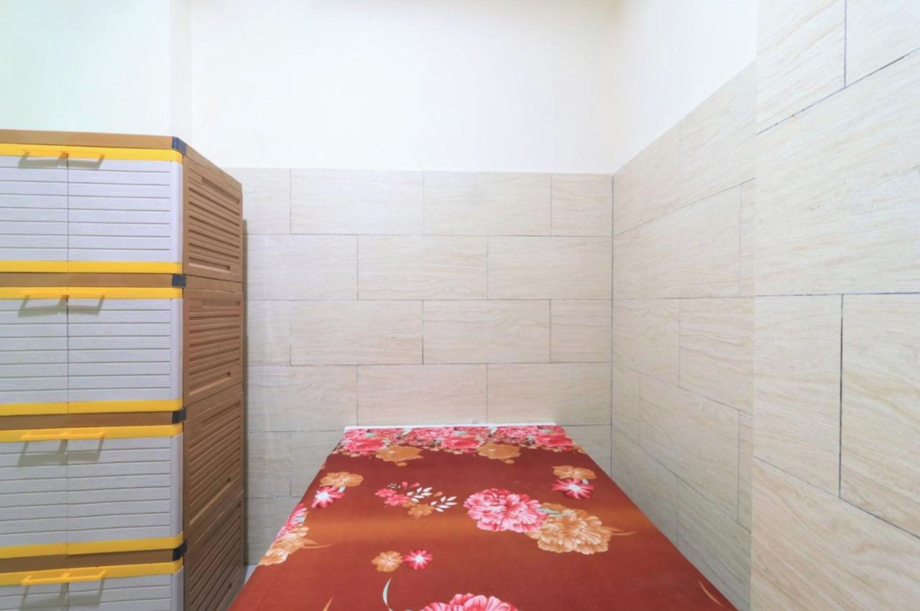 Een kleine kamer met een bed, een houten garderobe en betegelde wanden.