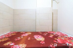 Een kamer met een bed voorzien van een bloemenprint sprei, lichte houten wanden en een effen wit plafond.