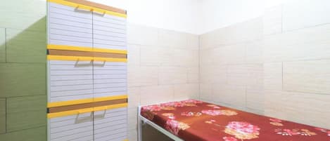 A small, single-bed room with a wooden wardrobe and a floral bedspread.