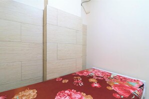 Un dormitorio con un armario de madera, una colcha estampada y una pared lisa.