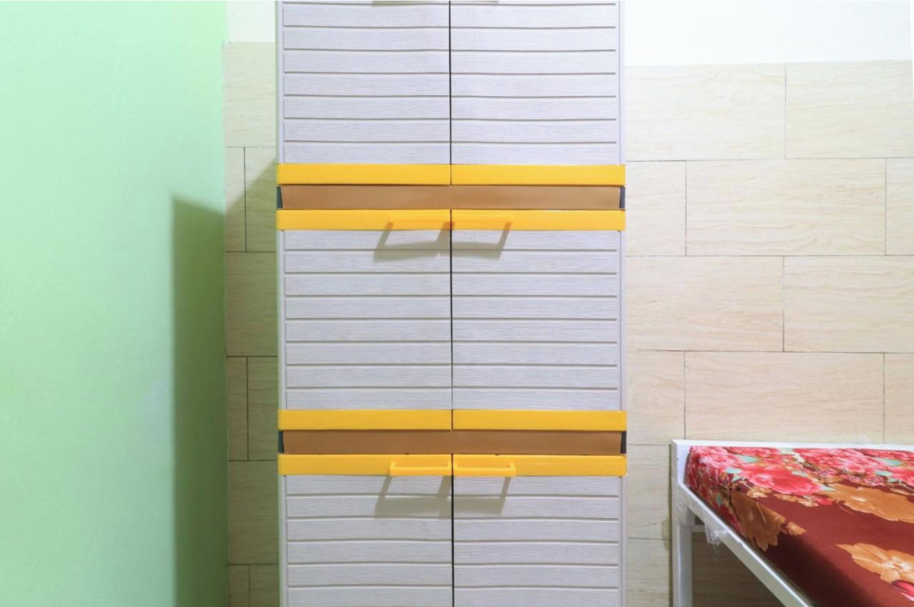A room with a grey wardrobe featuring yellow handles and a bed with a floral bedspread.